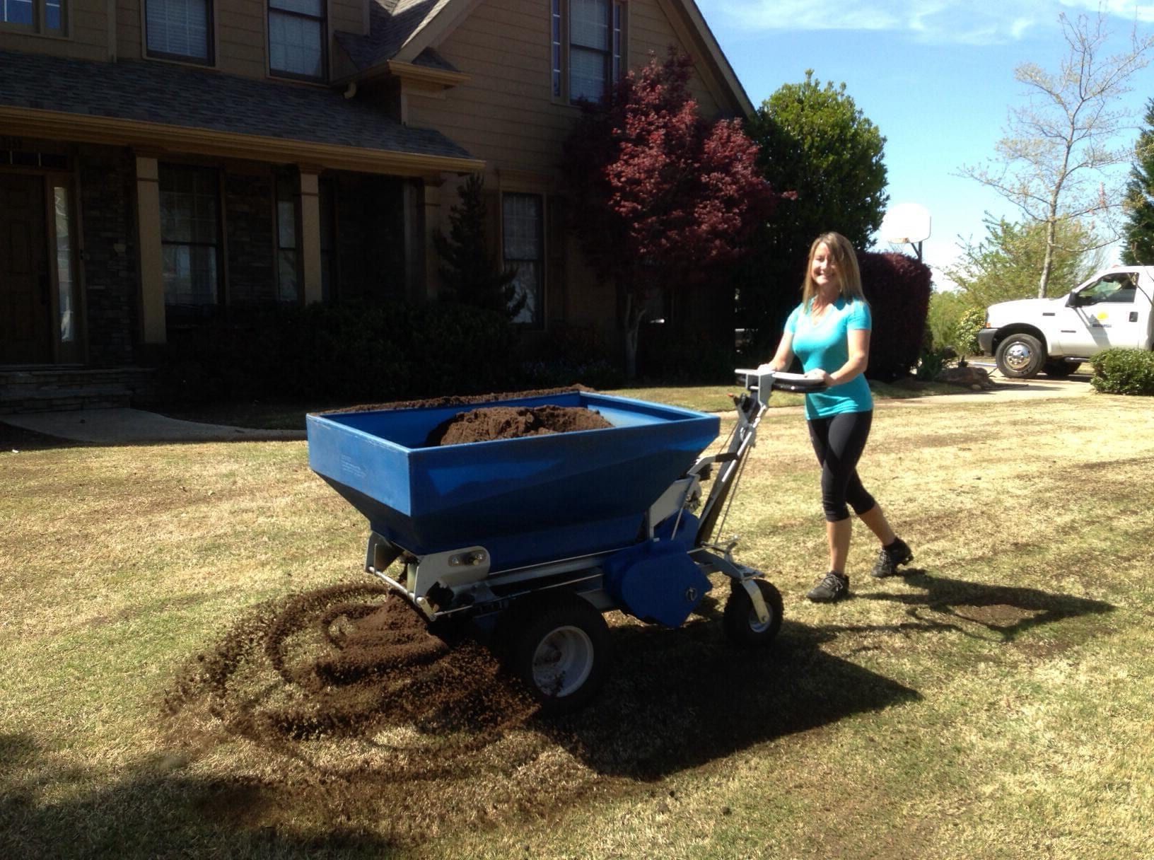 Spreading dark compost over a lawn with a walk-behind topdresser